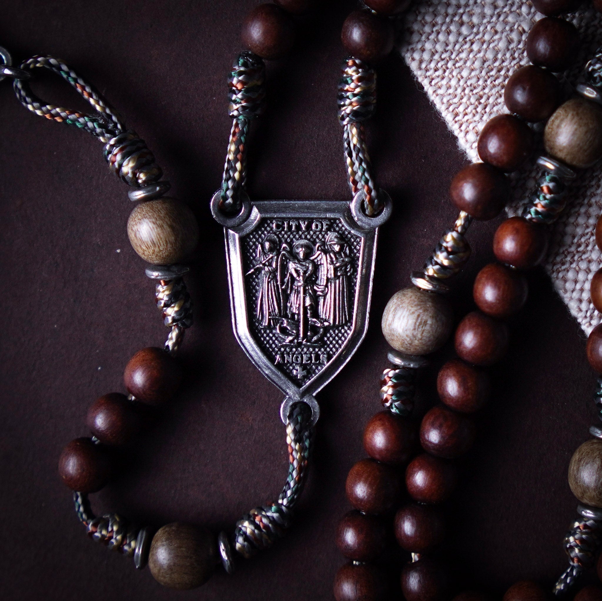 A shield-shaped silver rosary centerpiece with Saints Michael, Raphael, and Gabriel on it and the words “City of Angels.”