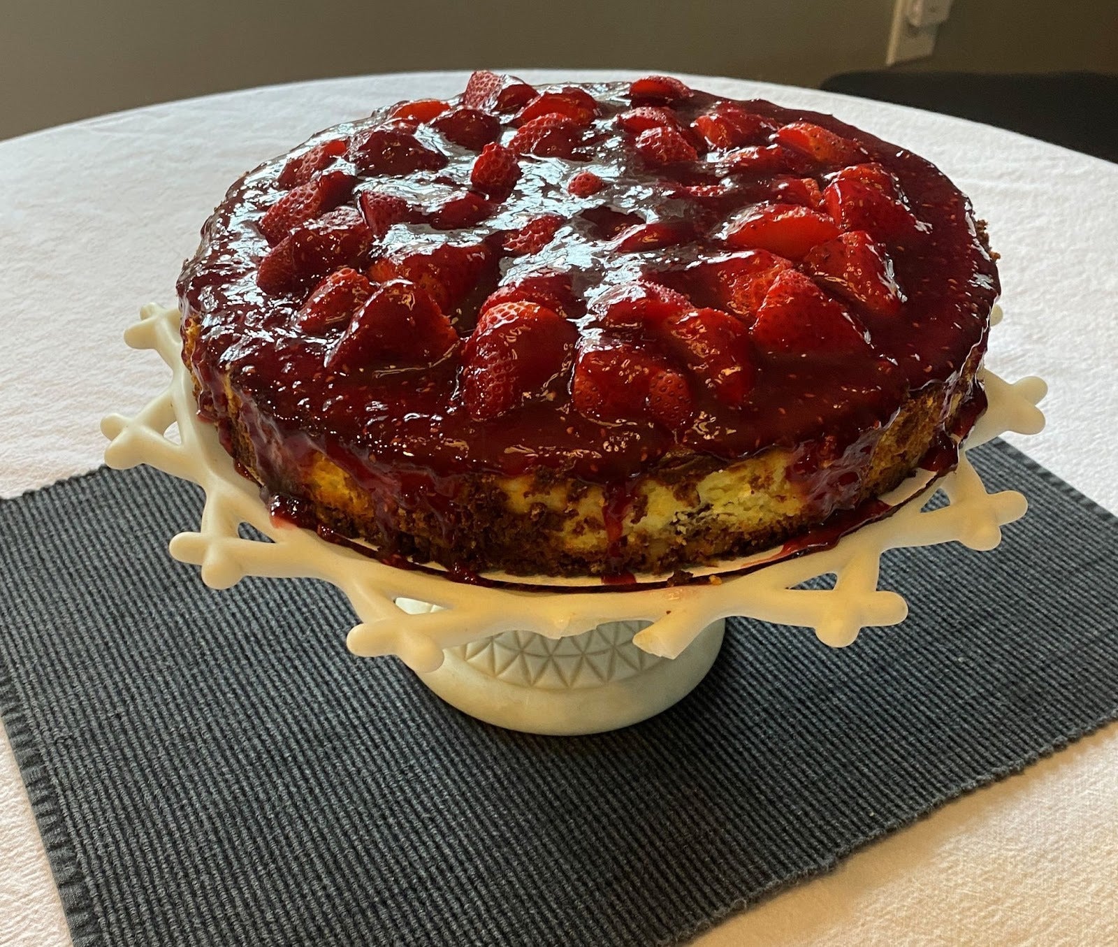A strawberry raspberry cheesecake on a white platter, topped with berries and a glaze for Thanksgiving dessert.