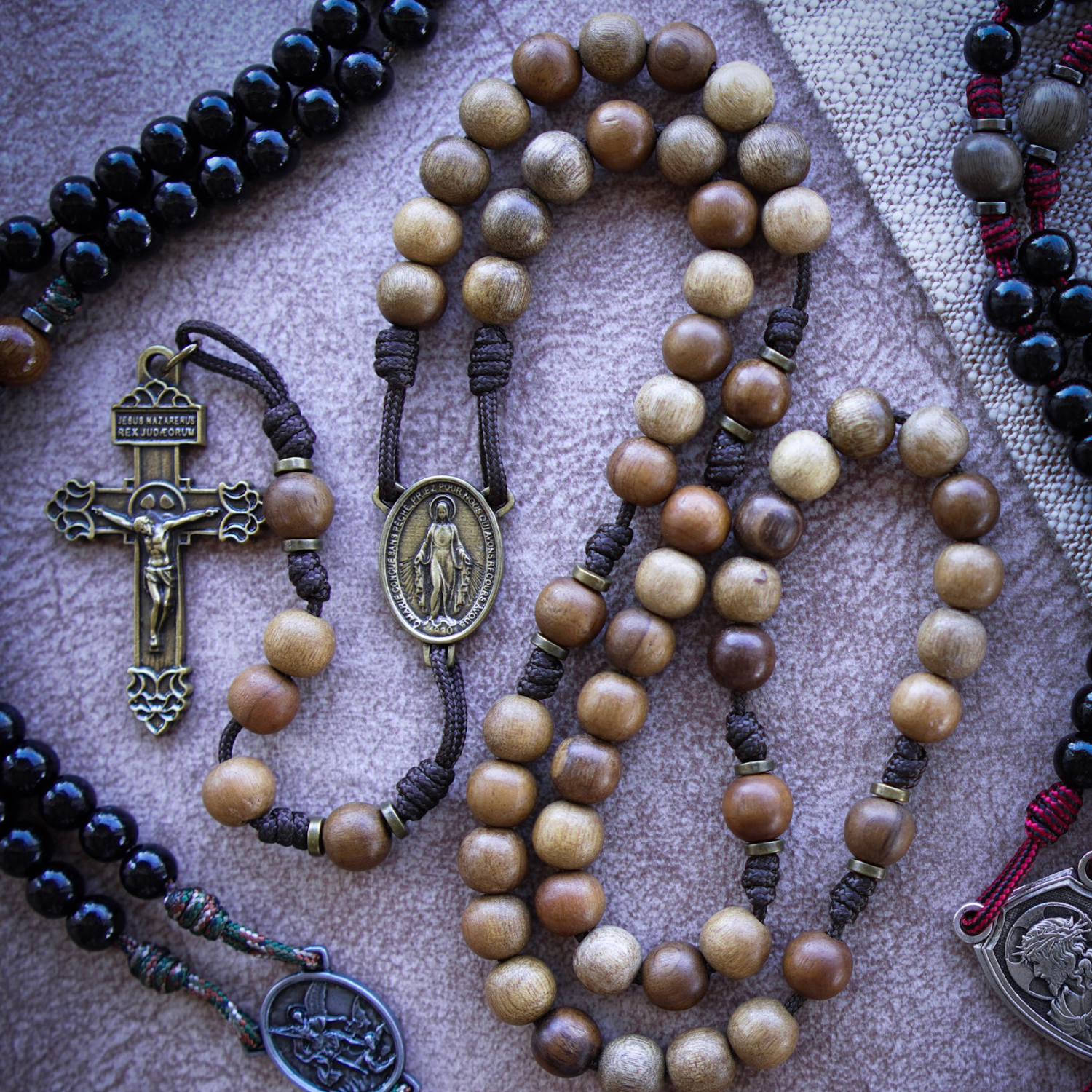 Flat lay collection of handcrafted Catholic rosaries, crucifixes, and religious jewelry on a dark linen background