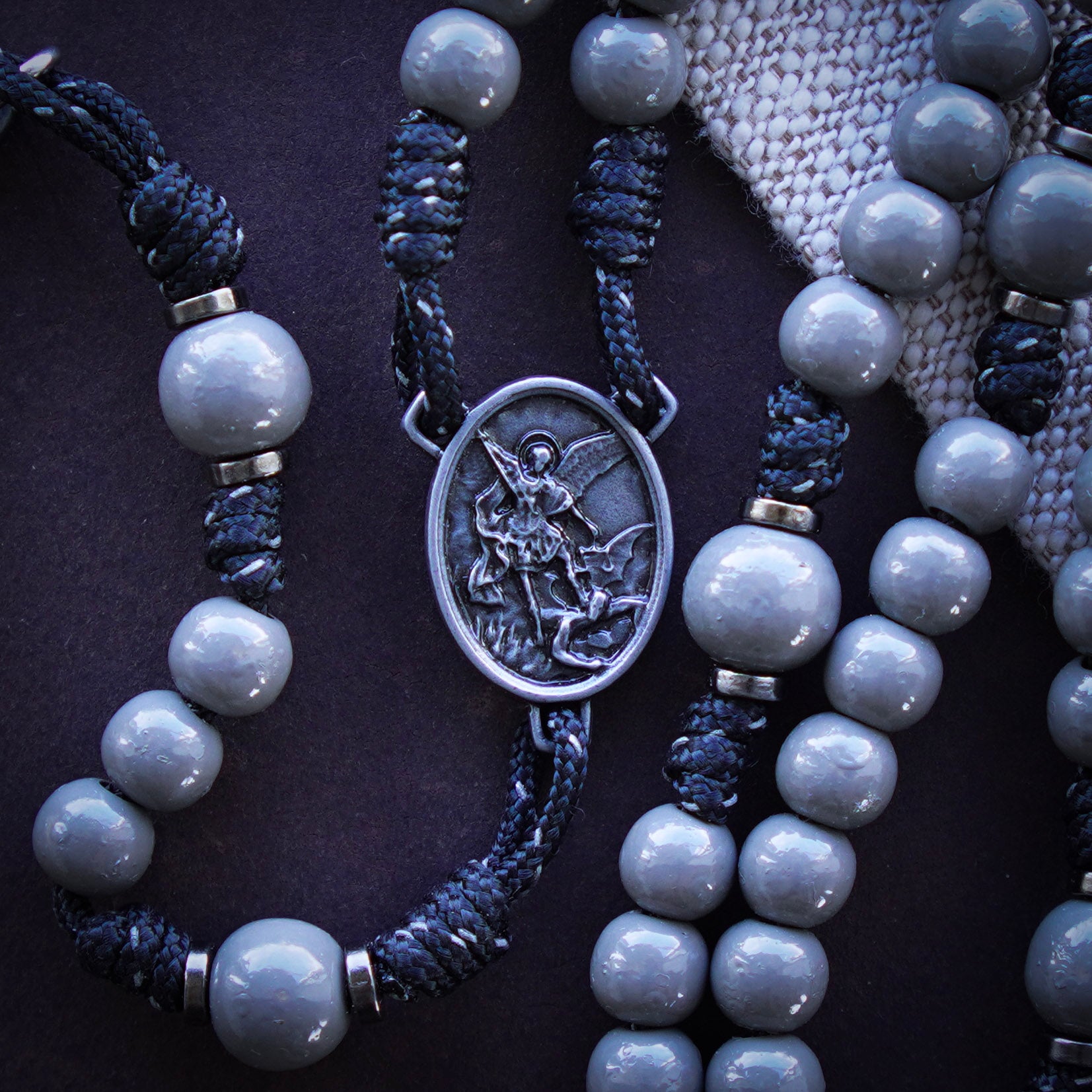 Close-up of a rosary with gray beads and a onyx centerpiece on a dark background