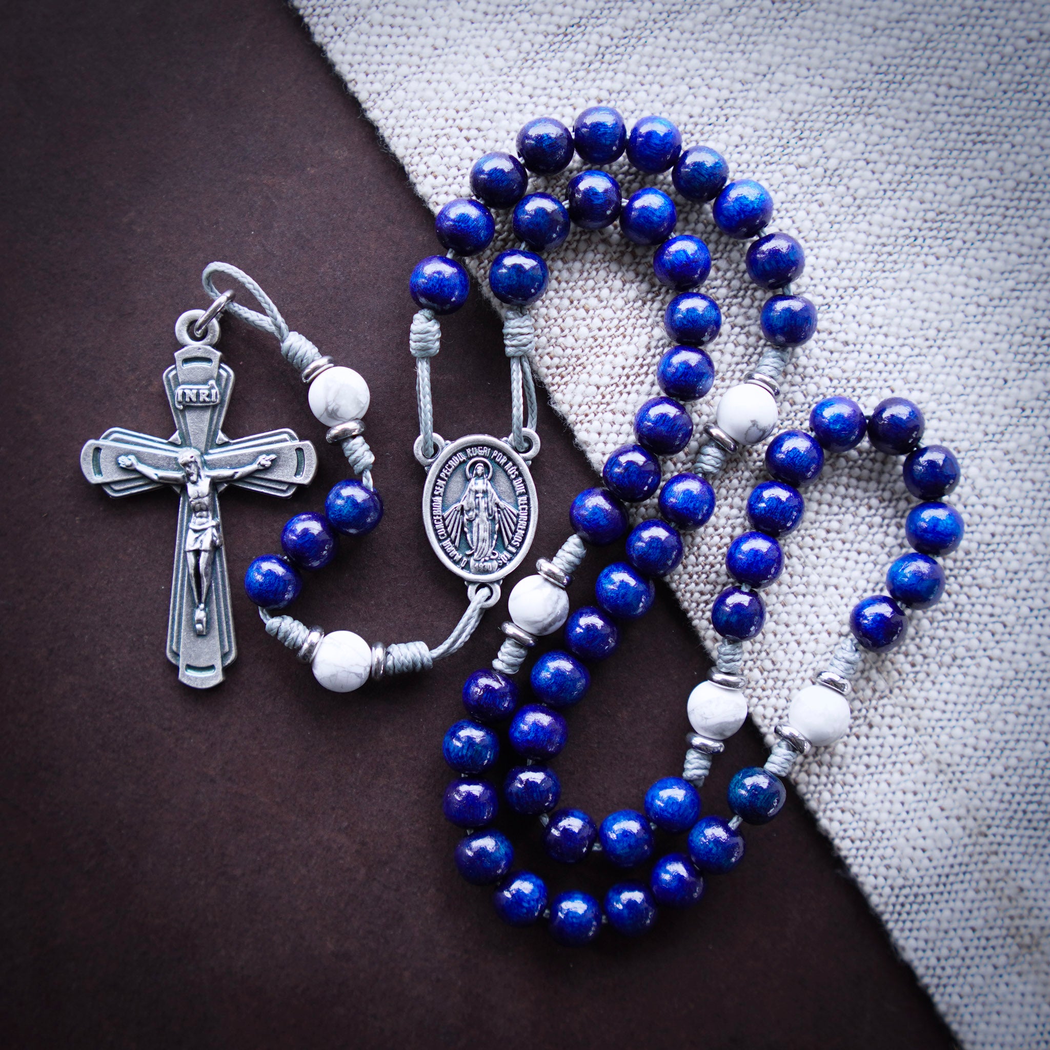Blue rosary with silver crucifix and medal on a dark surface