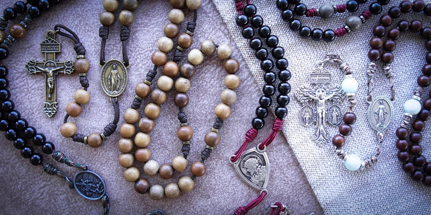 Flat lay collection of handcrafted Catholic rosaries, crucifixes, and religious jewelry on a dark linen background